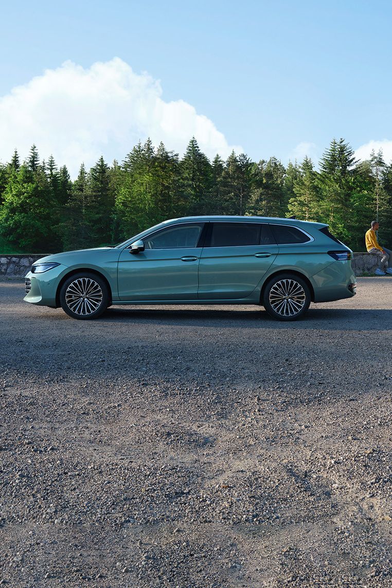 Seitenansicht eines grünen VW Passat Elegance vor einem Wald, im Hintergrund sieht man einen Mann und einen Jungen.