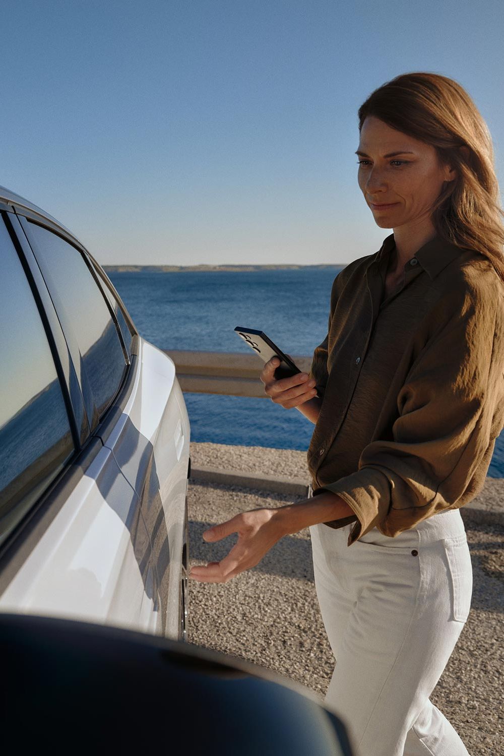 Eine Frau geht zu einem weißen VW ID.7 und öffnet die Tür. 