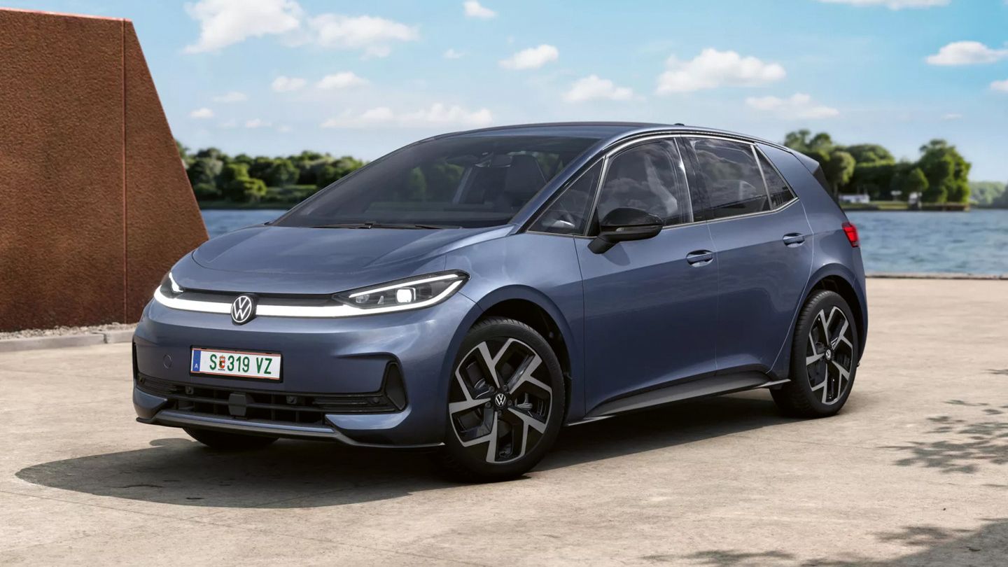 Blaugrauer ID.3 Neo steht auf einem Betonplatz an einem Gewässer mit Bäumen im Hintergrund. Die Front zeigt schmale LED-Scheinwerfer und das VW-Logo, die Felgen haben ein auffälliges, kantiges Design. Die Szene wirkt sonnig und ruhig.