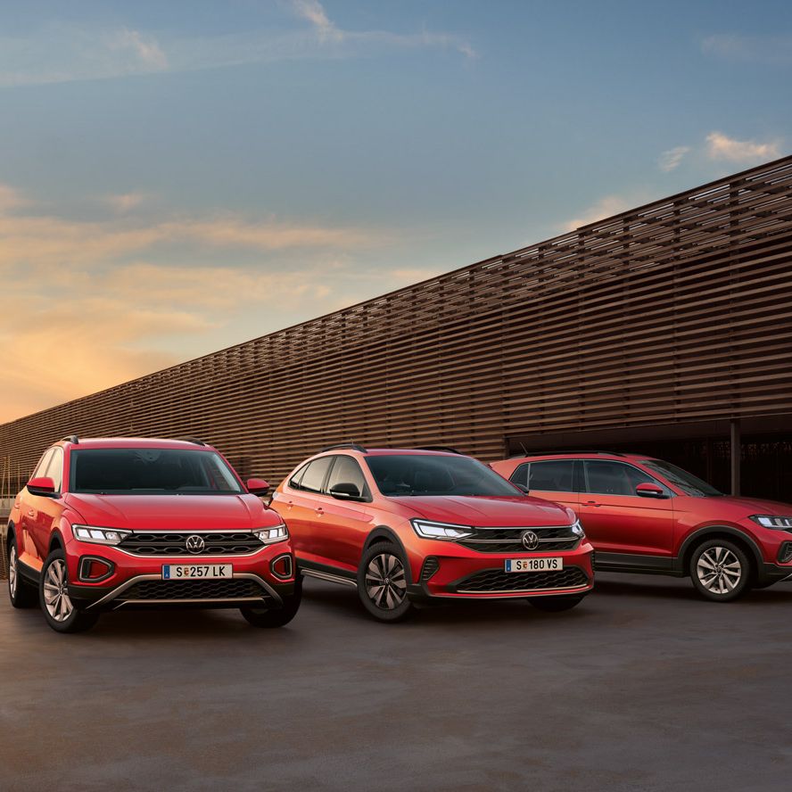 Drei rote VW Modelle, T-Roc, Taigo und T-Cross sind geparkt afugestellt neben einem langen Gebäude