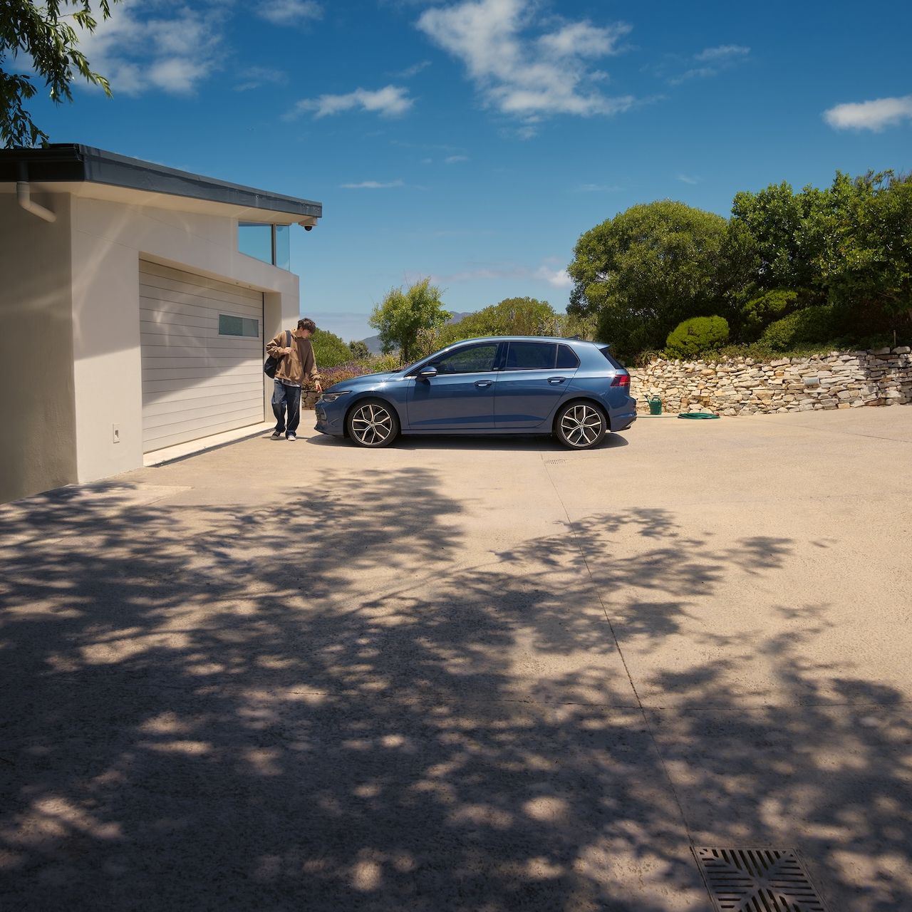 Ein junger Mann geht an einem blauen VW Golf vorbei