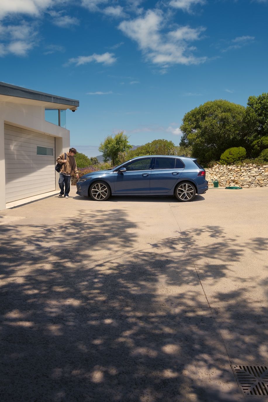 Ein junger Mann geht an einem blauen VW Golf vorbei