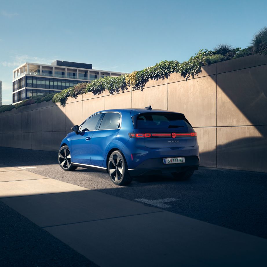 Ein blauer VW ID. Polo Style steht am Straßenrand vor einer begrünten Mauer.