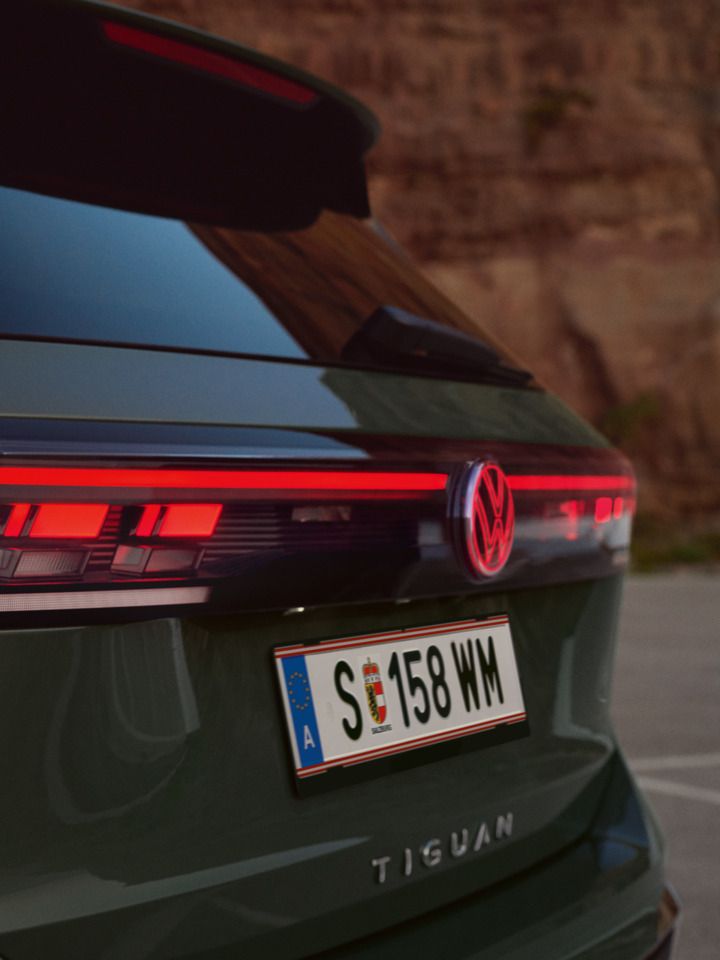 Detailansicht der Heck-Lichtsignatur eines vor einer felsigen Landschaft geparkten dunkelgrünen VW Tiguan.