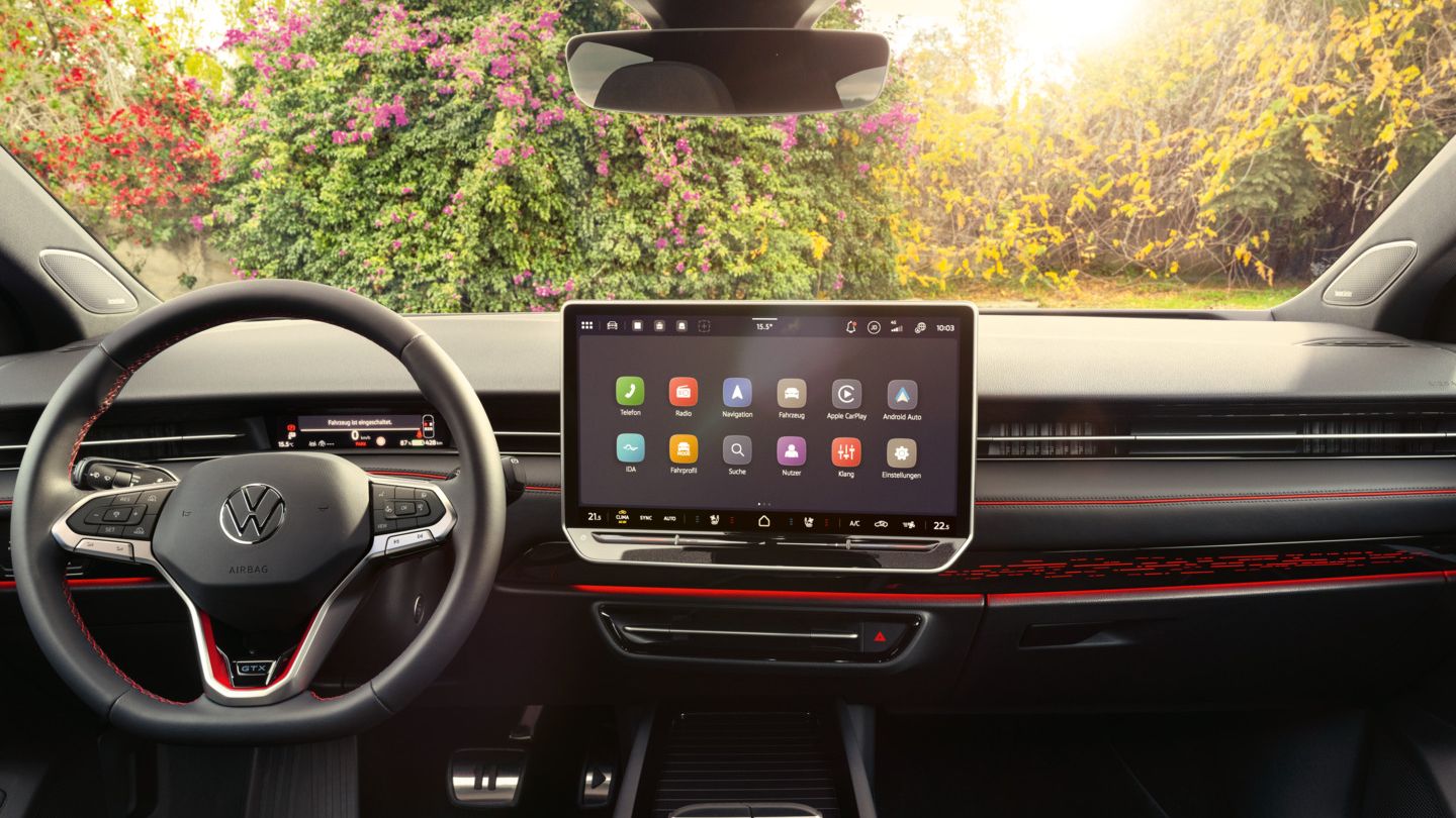 Interieur des ID.7 GTX mit roter Ambientebeleuchtung, roten Ziernähten am Multifunktionslenkrad und dem Infotainmentsystem. 