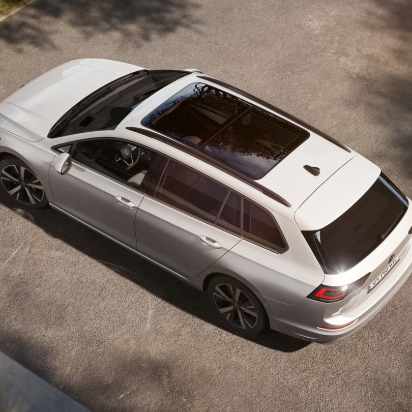 Das Bild zeigt einen Golf Variant, der auf einem gepflasterten Parkplatz steht. Der Wagen hat ein großes, dunkles Panoramadach. Die Perspektive ist von oben aufgenommen.