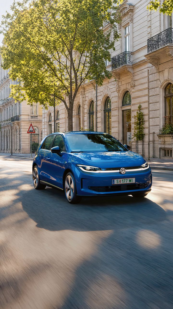 Ein blauer VW ID. Polo fährt auf einer breiten Straße im Schatten einer Allee.