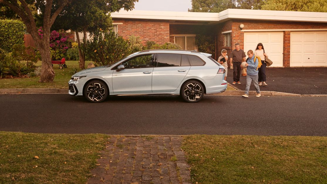 Ein weißer VW Golf Variant parkt vor einem Bungalow in einer Wohnstraße mit Bäumen. 