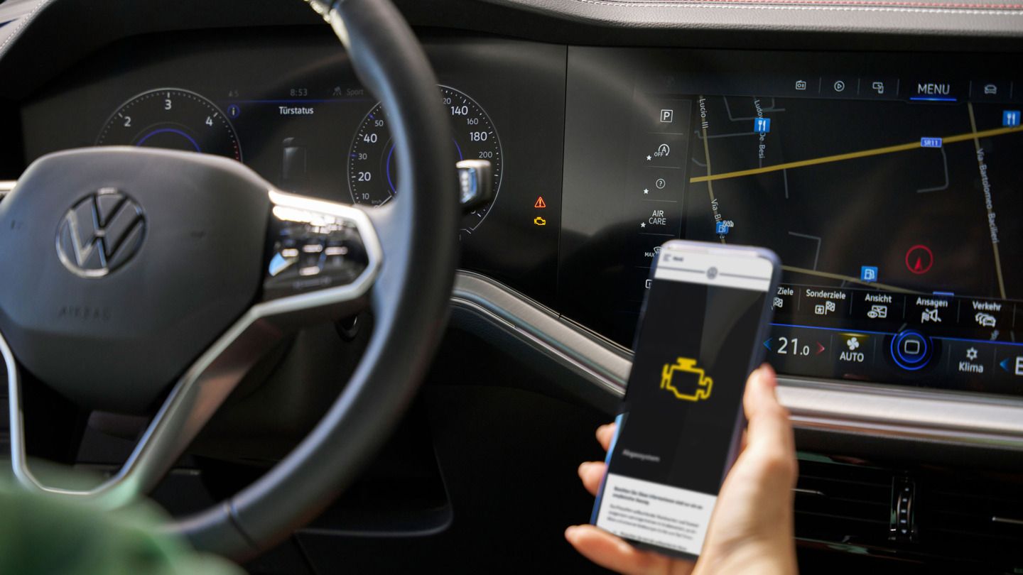 Nahaufnahme VW-Cockpit, im Vordergrund ein Smartphone mit Informationen über eine Warnleuchte