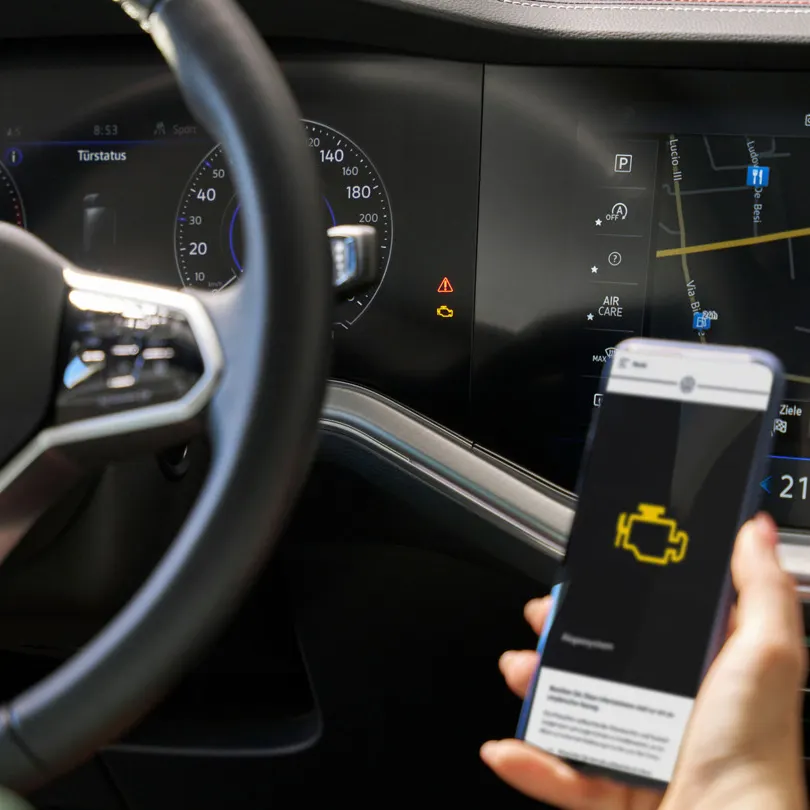 Nahaufnahme VW-Cockpit, im Vordergrund ein Smartphone mit Informationen über eine Warnleuchte
