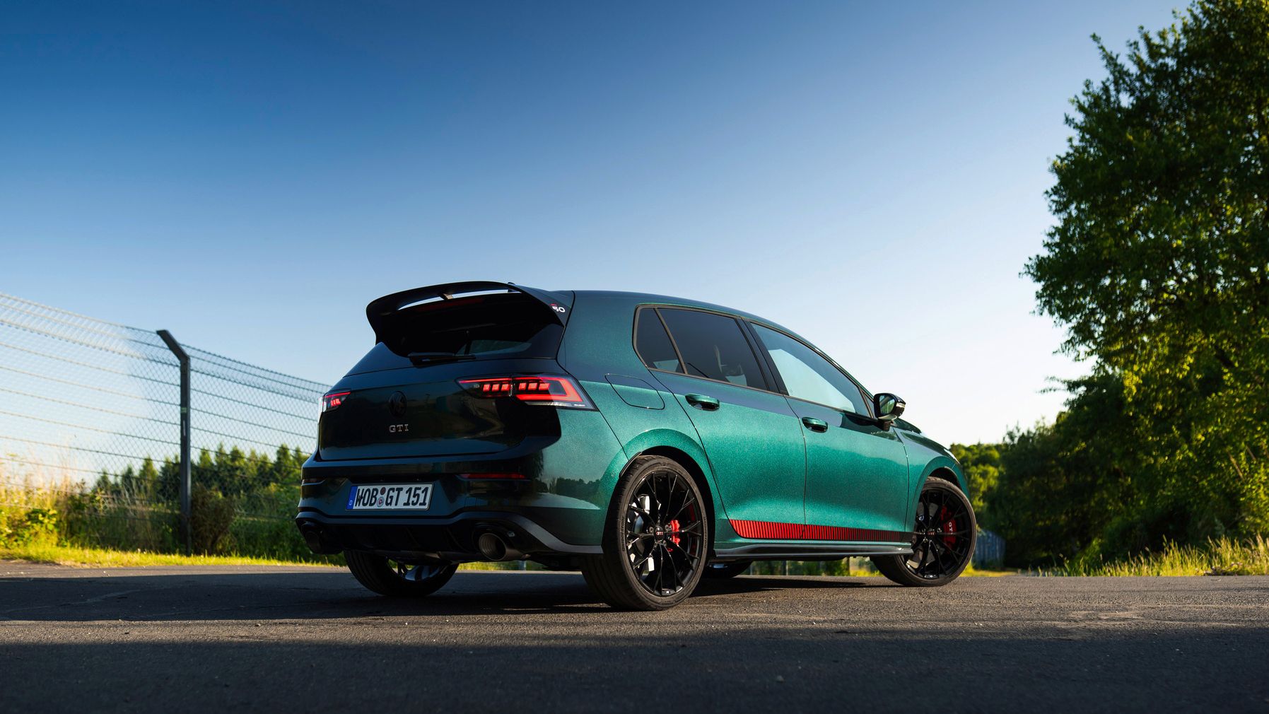 Seitenansicht und Heck eines moosgrünen VW Golf GTI EDITION 50, der auf einer Straße steht.