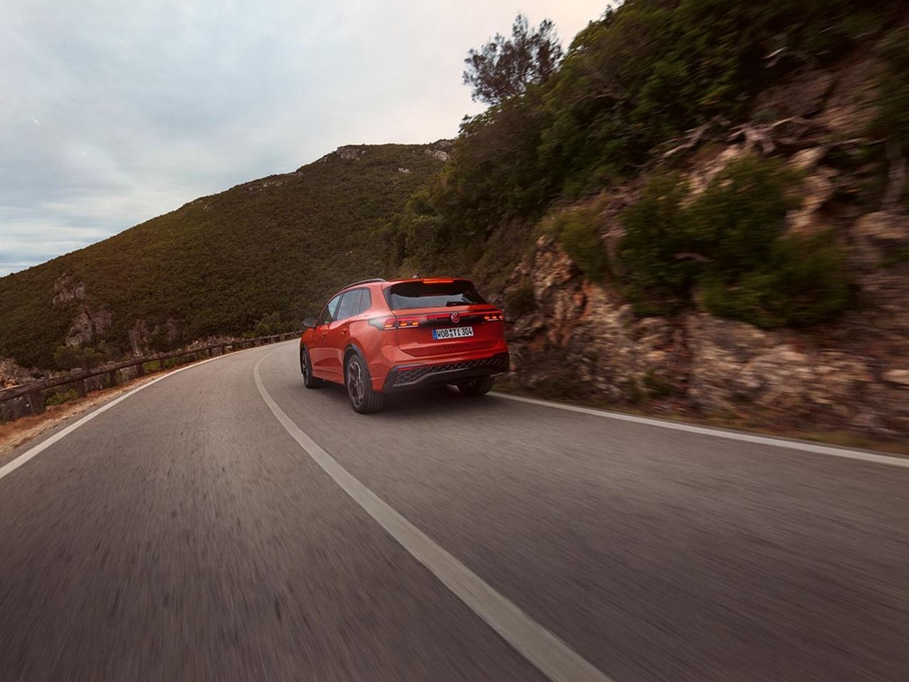 Roter VW Tiguan in Heckansicht fährt durch eine bergige Landschaft.