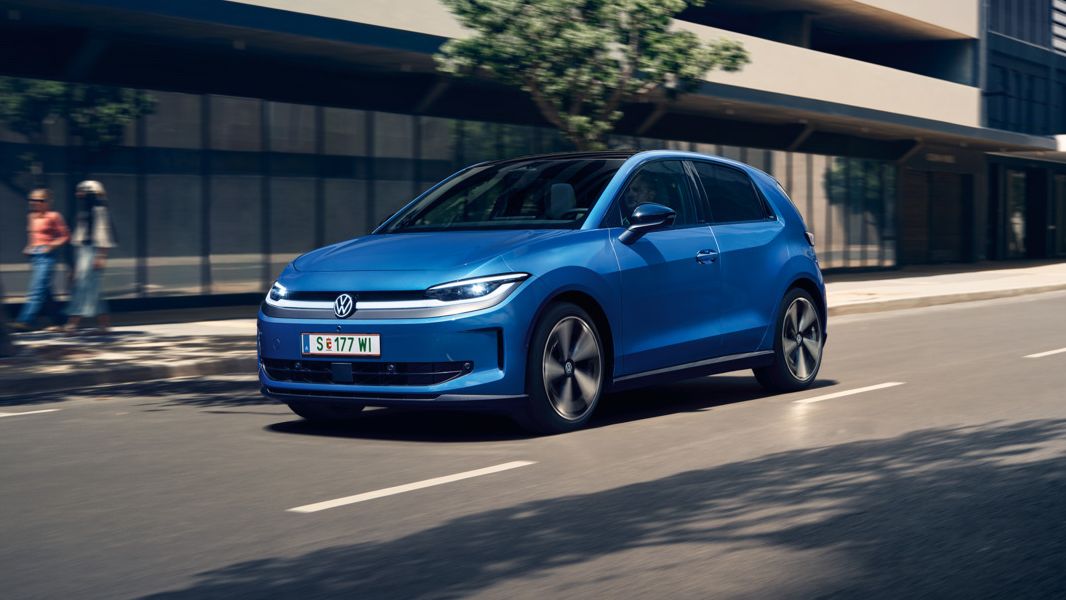 Ein blauer VW ID. Polo Style fährt durch eine Stadt mit grünen Bäumen am Straßenrand.