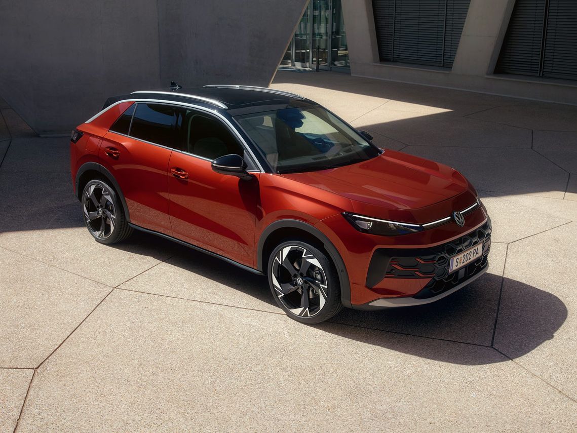 Ein roter VW T-Roc Style steht vor einem modernen Gebäude im Sonnenlicht