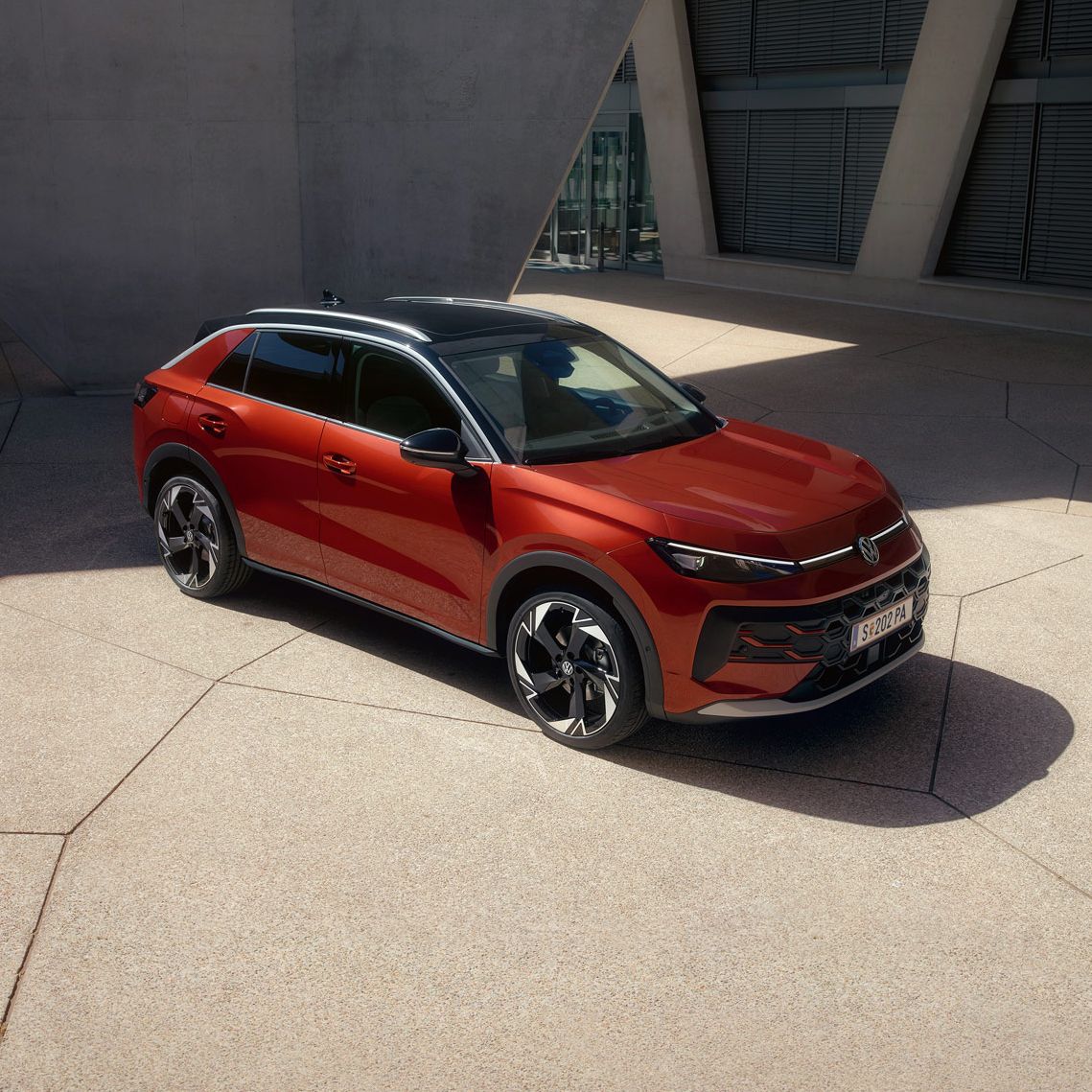 Ein roter VW T-Roc Style steht vor einem modernen Gebäude im Sonnenlicht
