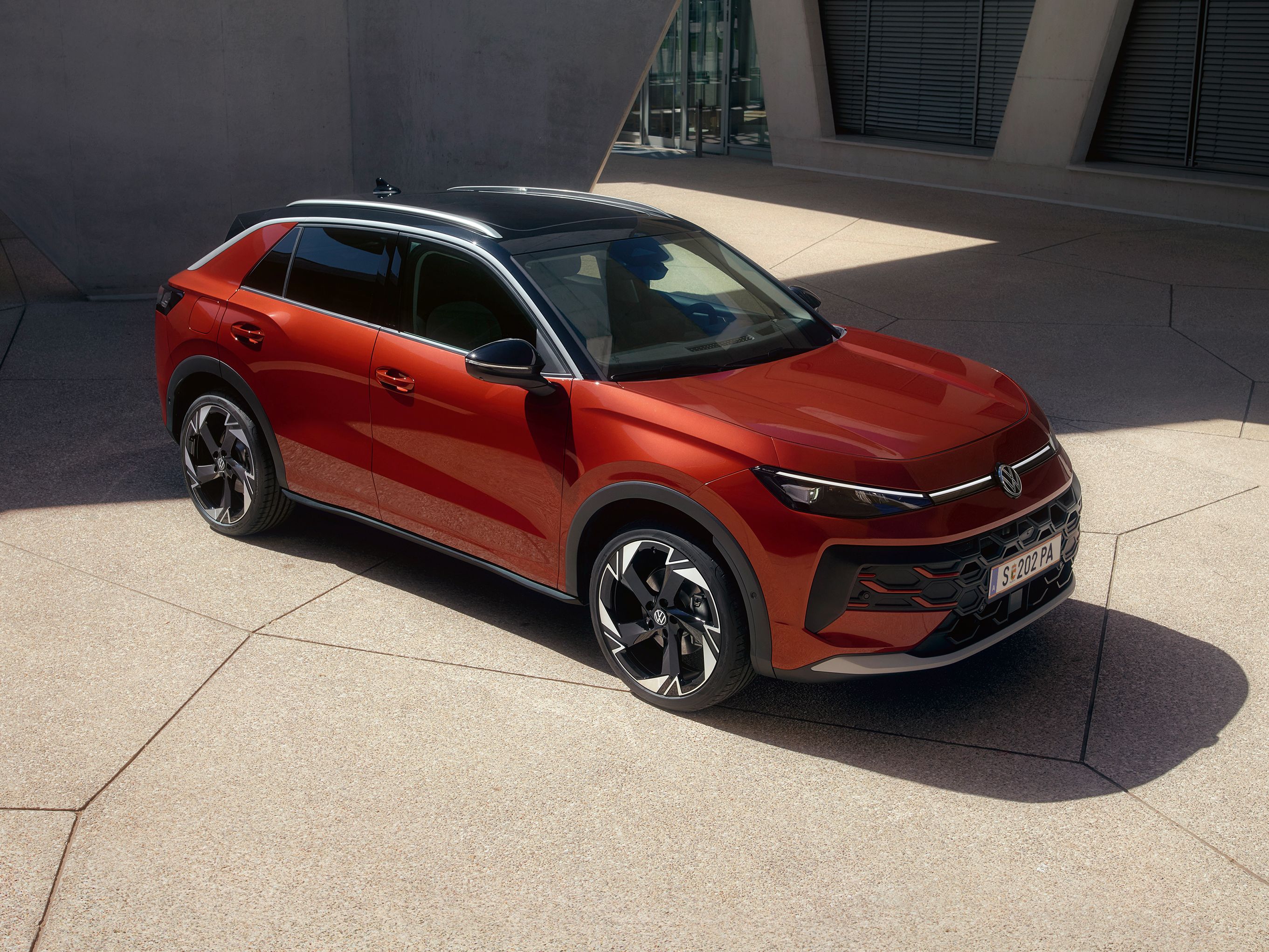 Ein roter VW T-Roc Style steht vor einem modernen Gebäude im Sonnenlicht