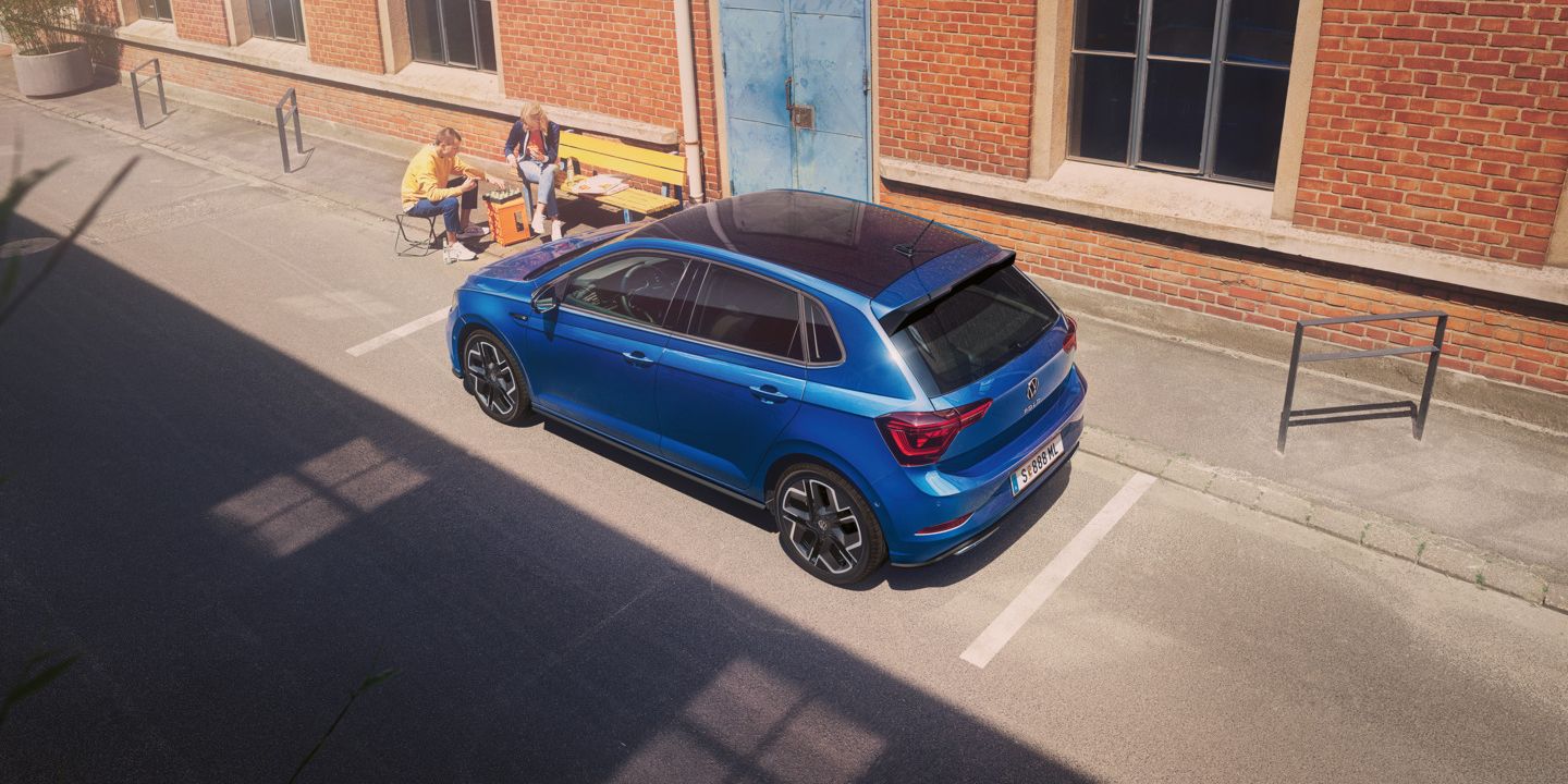 Blick von schräg oben auf einen parkenden VW Polo R-Line mit Roof-Pack, neben dem Auto spielt ein Pärchen Schach.