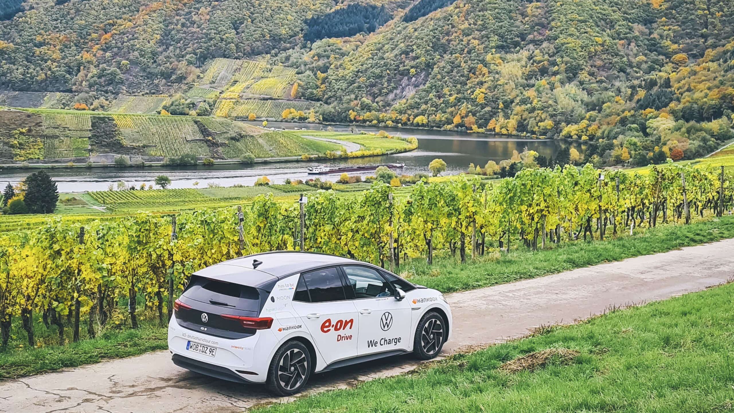 Ein ID.3 fährt auf einer Straße inmitten grüner Weinberge. Im Hintergrund fließt ein Fluss durch die malerischen Hügel. Die Landschaft zeigt Herbstfarben.