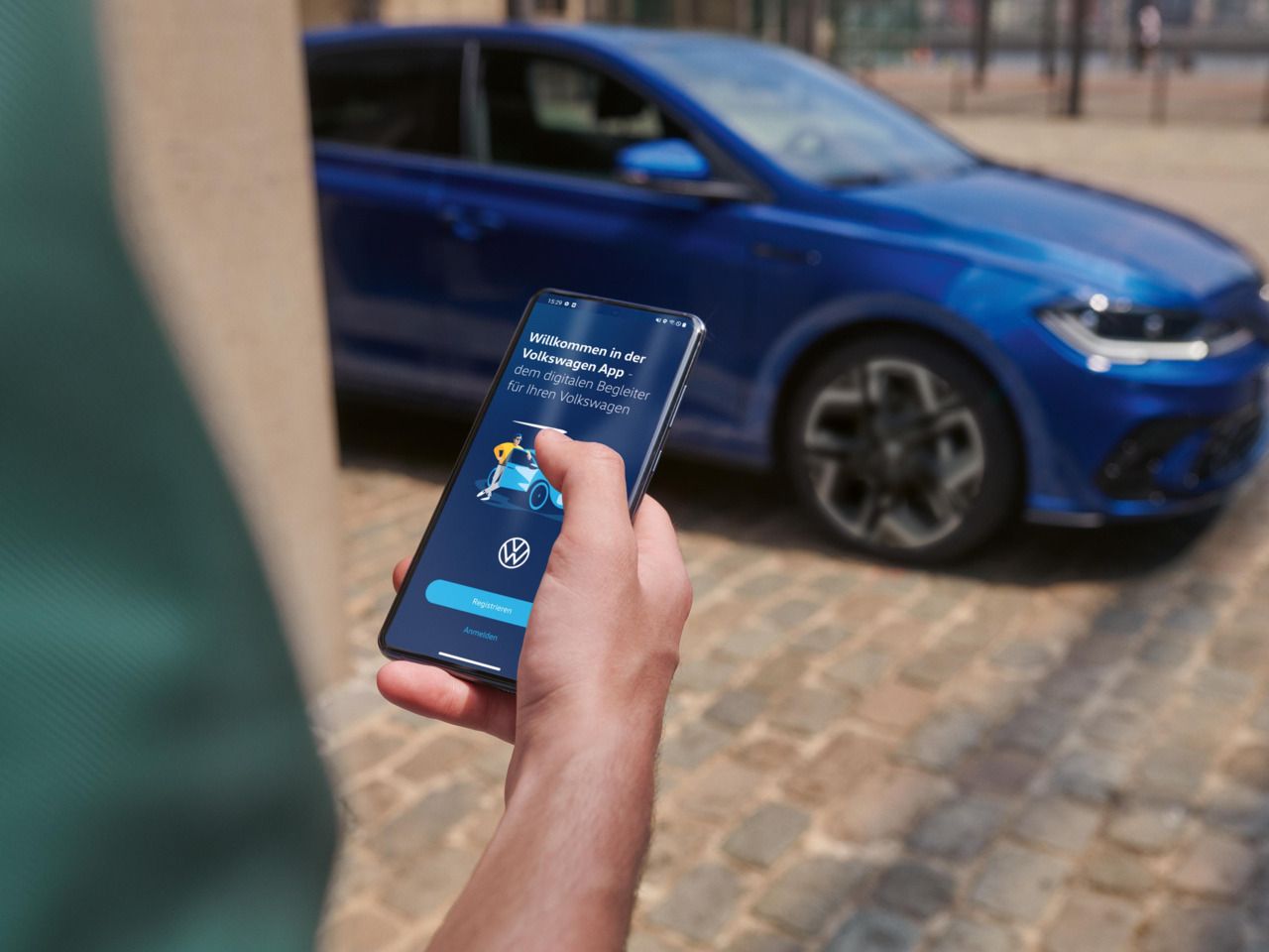 Eine Person hält ein Smartphone in der Hand mit der Volkswagen App, im Hintergrund steht ein blauer VW Polo R-Line.