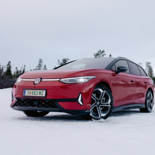 Ein roter ID.7 steht auf einer verschneiten Fläche, umgeben von vereinzelt stehenden Nadelbäumen. Die Umgebung wirkt kühl und winterlich. Der Himmel ist bewölkt und es herrscht eine ruhige Atmosphäre.