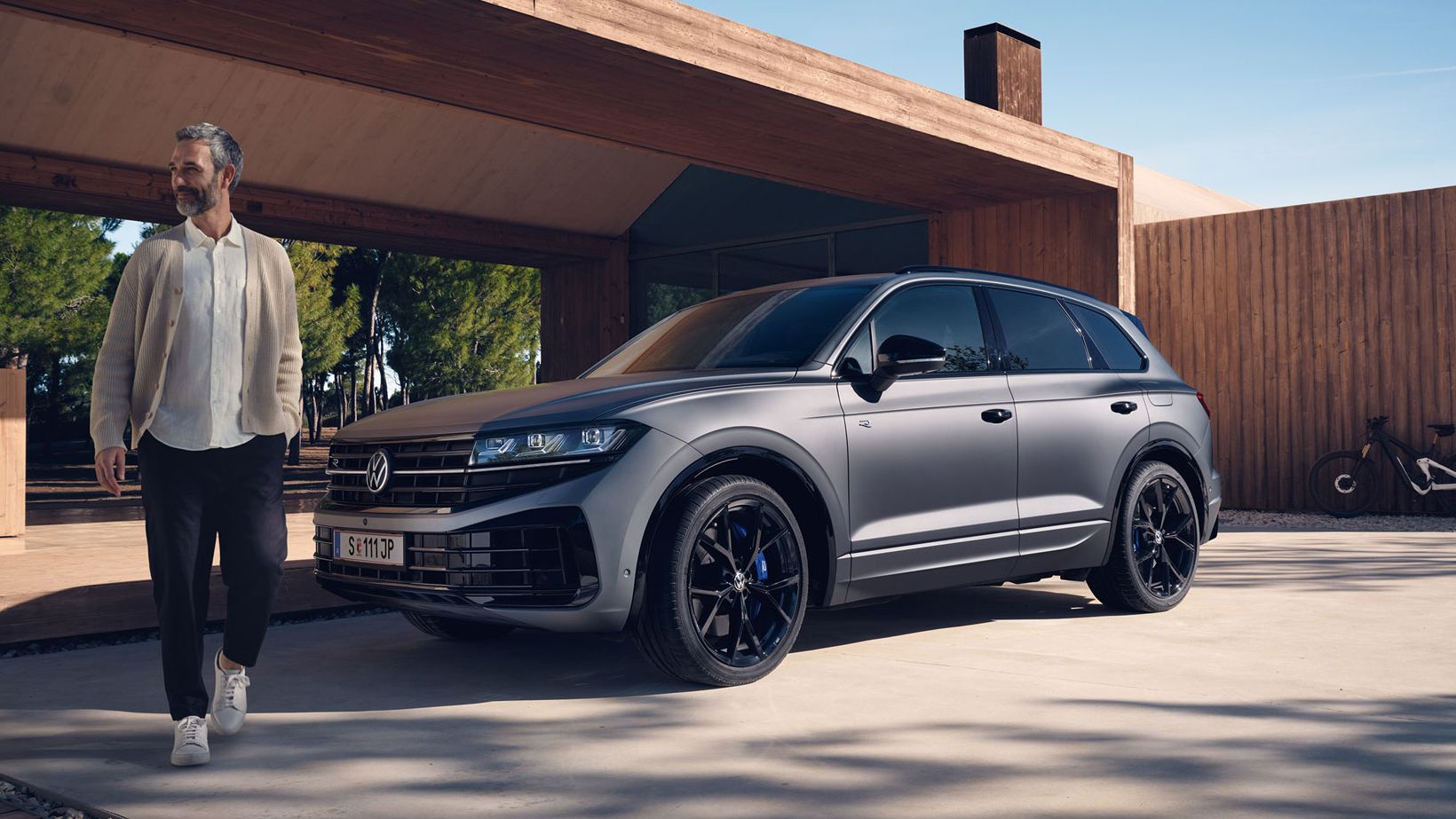 Ein VW Touareg R eHybrid parkt vor einem Haus, ein Mann bewegt sich vom Fahrzeug fort