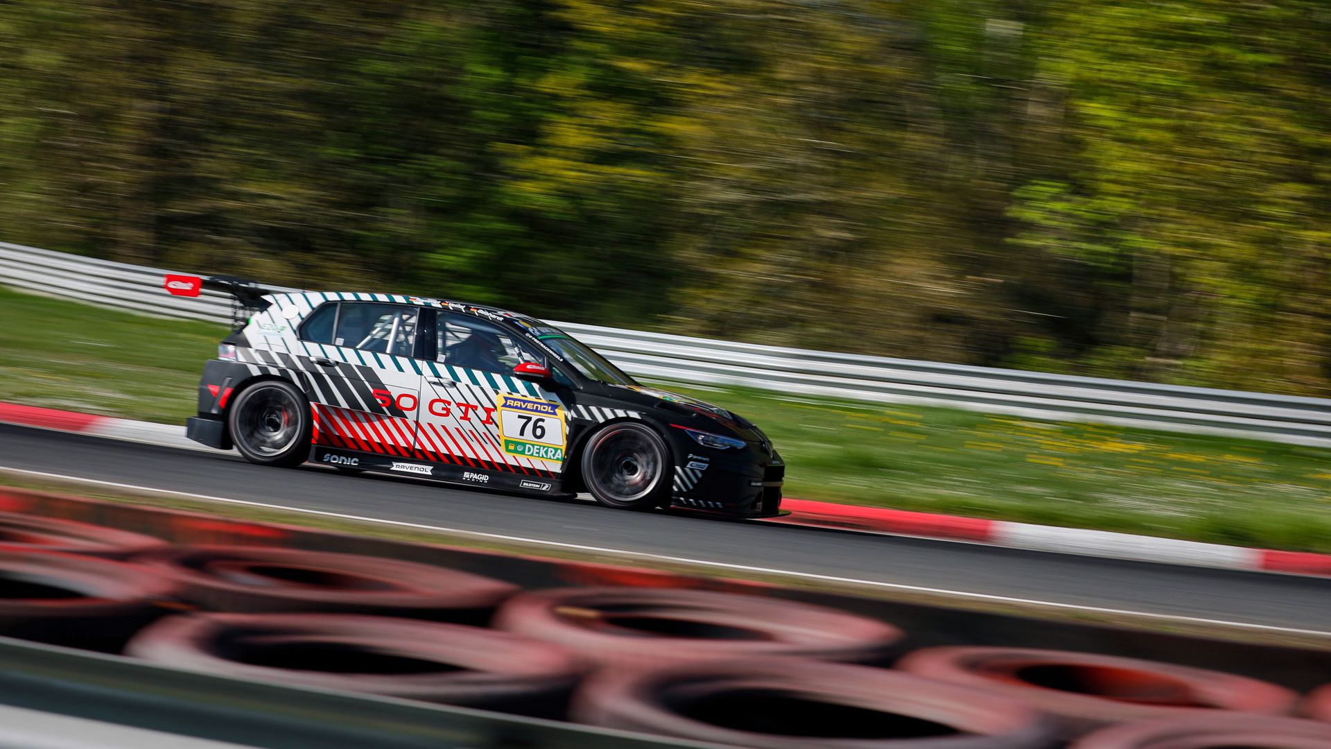 Ein Golf GTI Clubsport mit der Nummer 76 fährt schnell auf einer Rennstrecke. Der Hintergrund ist verschwommen, da der Wagen in Bewegung ist. Die Reifen am Streckenrand sind gut sichtbar.