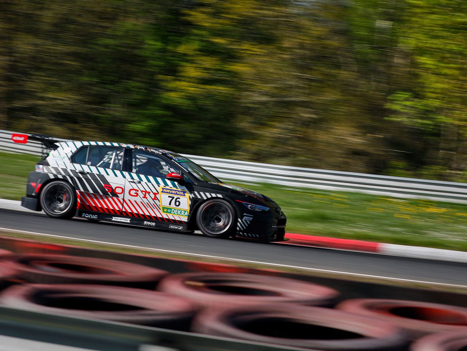 Ein Golf GTI Clubsport mit der Nummer 76 fährt schnell auf einer Rennstrecke. Der Hintergrund ist verschwommen, da der Wagen in Bewegung ist. Die Reifen am Streckenrand sind gut sichtbar.
