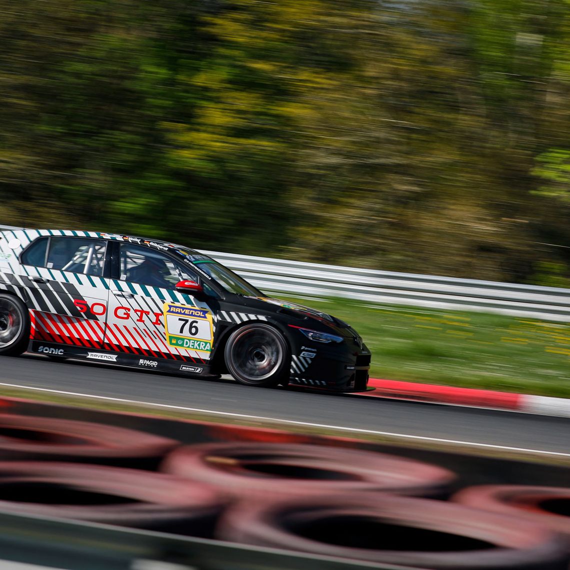 Ein Golf GTI Clubsport mit der Nummer 76 fährt schnell auf einer Rennstrecke. Der Hintergrund ist verschwommen, da der Wagen in Bewegung ist. Die Reifen am Streckenrand sind gut sichtbar.