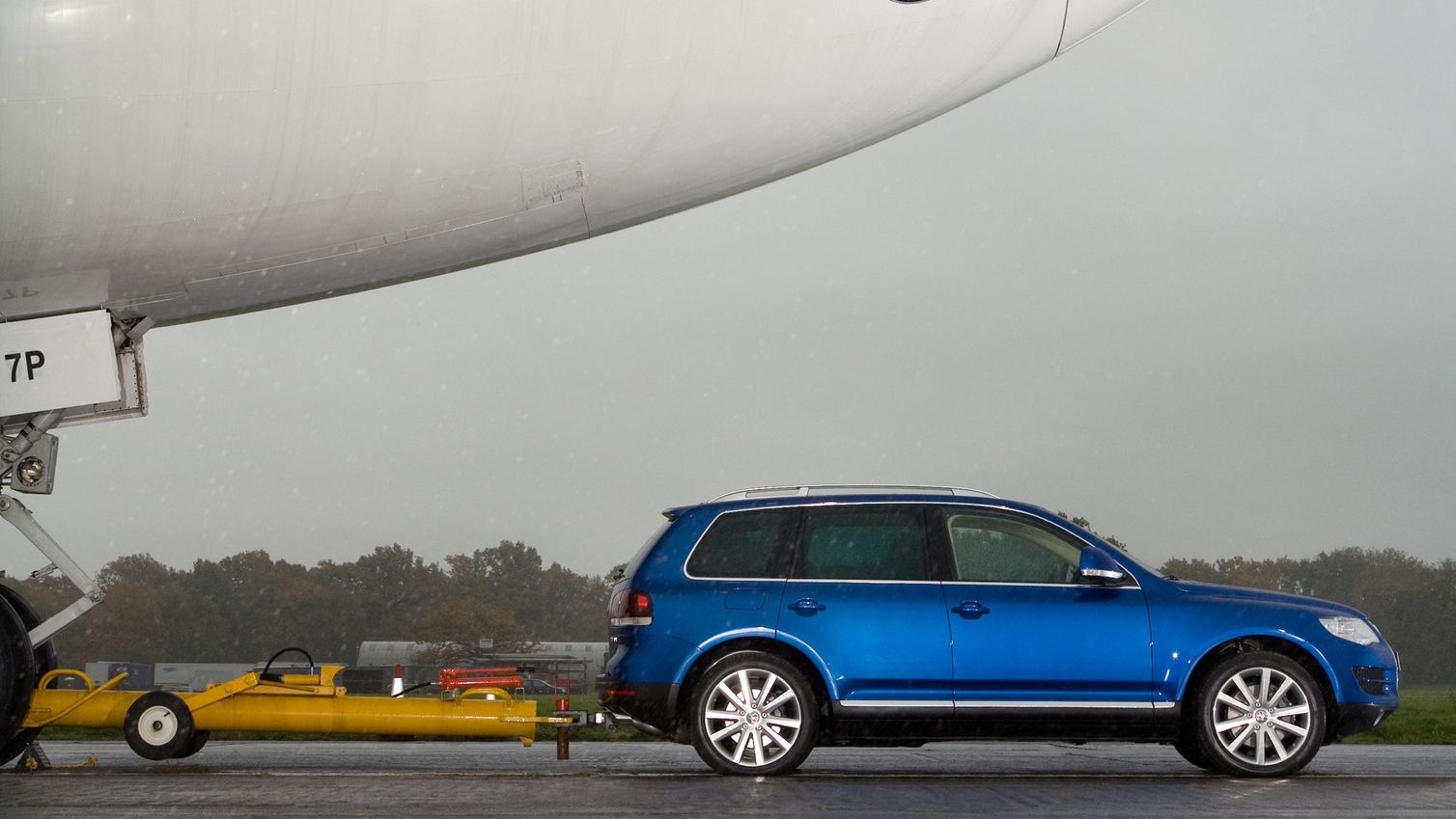 Ein blauer Touareg zieht ein großes Flugzeug per Anhängekupplung.