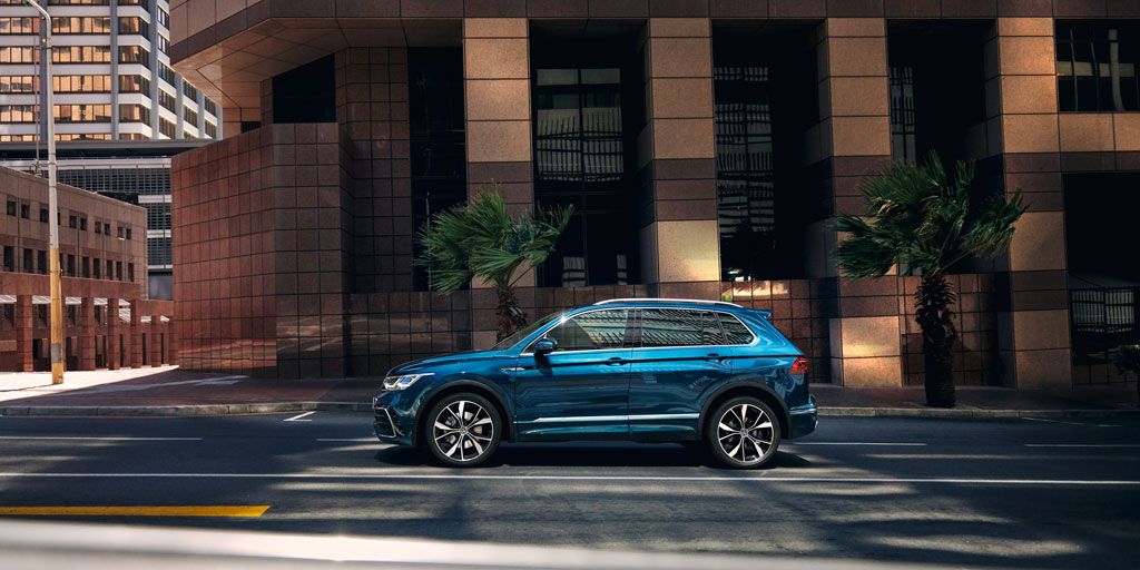 VW Tiguan steht seitlich vor Hochhaus mit großen Fenstern, mit der optionalen 4MOTION Active Control sind verschiedene Fahrprofile auswählbar.