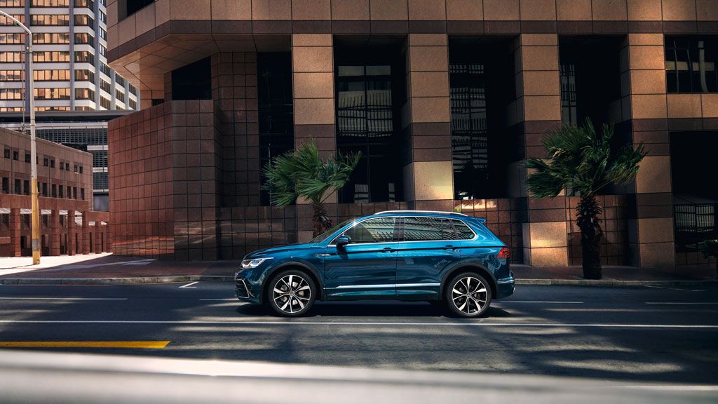 VW Tiguan steht seitlich vor Hochhaus mit großen Fenstern, mit der optionalen 4MOTION Active Control sind verschiedene Fahrprofile auswählbar.