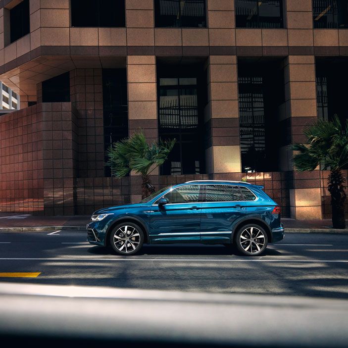 VW Tiguan steht seitlich vor Hochhaus mit großen Fenstern, mit der optionalen 4MOTION Active Control sind verschiedene Fahrprofile auswählbar.