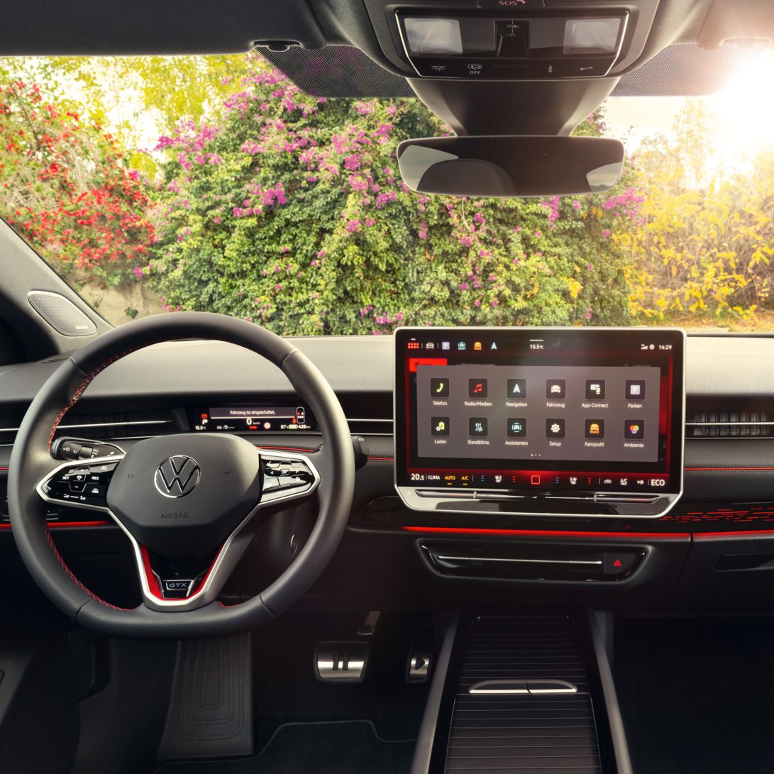 Cockpit eines VW ID.7 GTX mit Multifunktionslenkrad und Infotainmentsystem mit roten Akzenten.