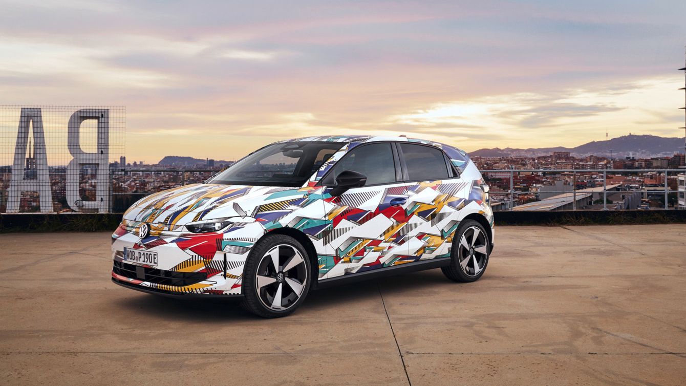 Ein bunt bemalter ID. Polo steht auf einem Parkplatz mit Stadt und Hügeln im Hintergrund. Das Fahrzeug ist mit einem lebhaften, abstrakten Design bedeckt. Der Himmel ist teils bewölkt mit Sonnenaufgang oder Sonnenuntergang Farben.