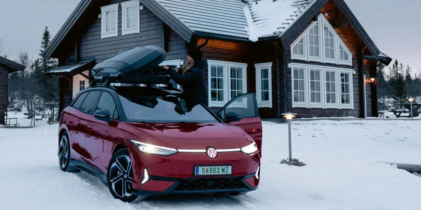Ein roter ID.7 Tourer GTX mit Dachbox steht im Schnee vor einem Wohnhaus. 