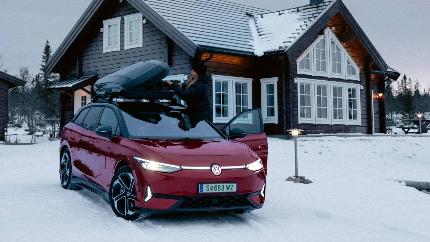 Ein roter ID.7 Tourer GTX mit Dachbox steht im Schnee vor einem Wohnhaus. 