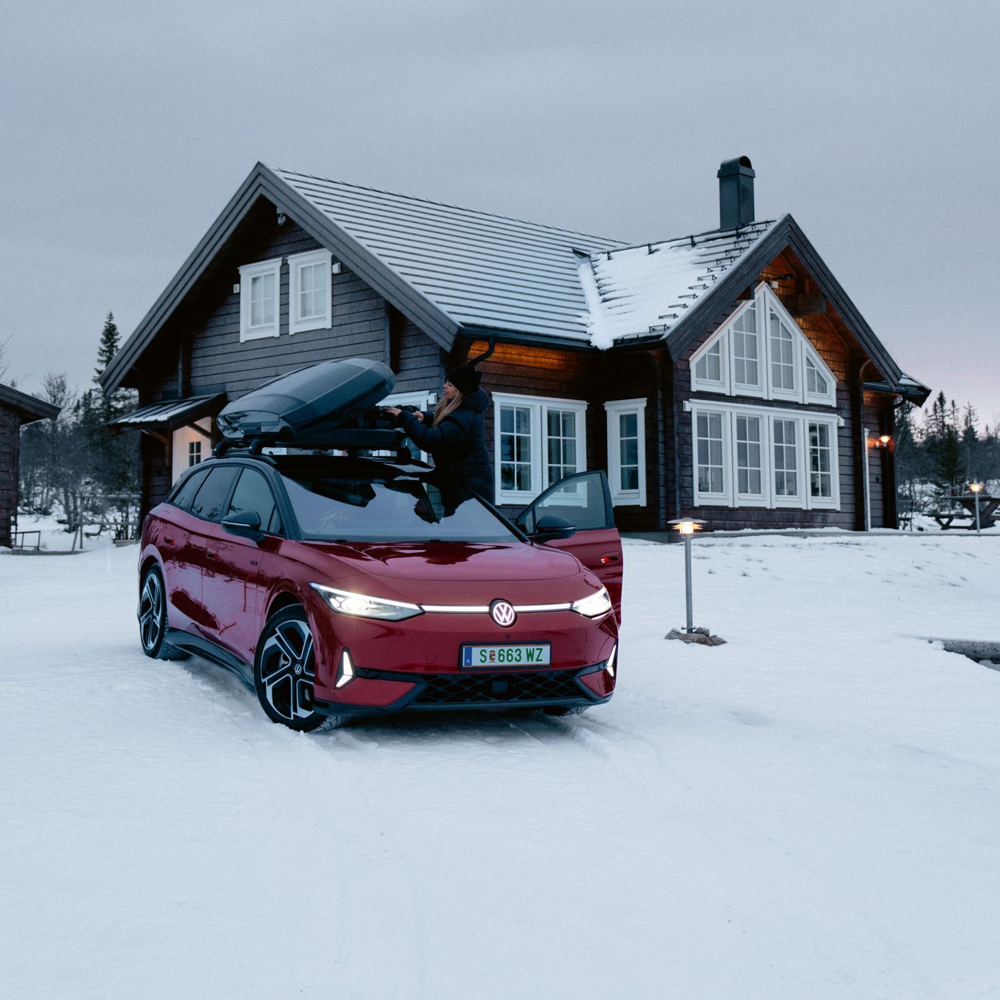 Ein roter ID.7 Tourer GTX mit Dachbox steht im Schnee vor einem Wohnhaus. 