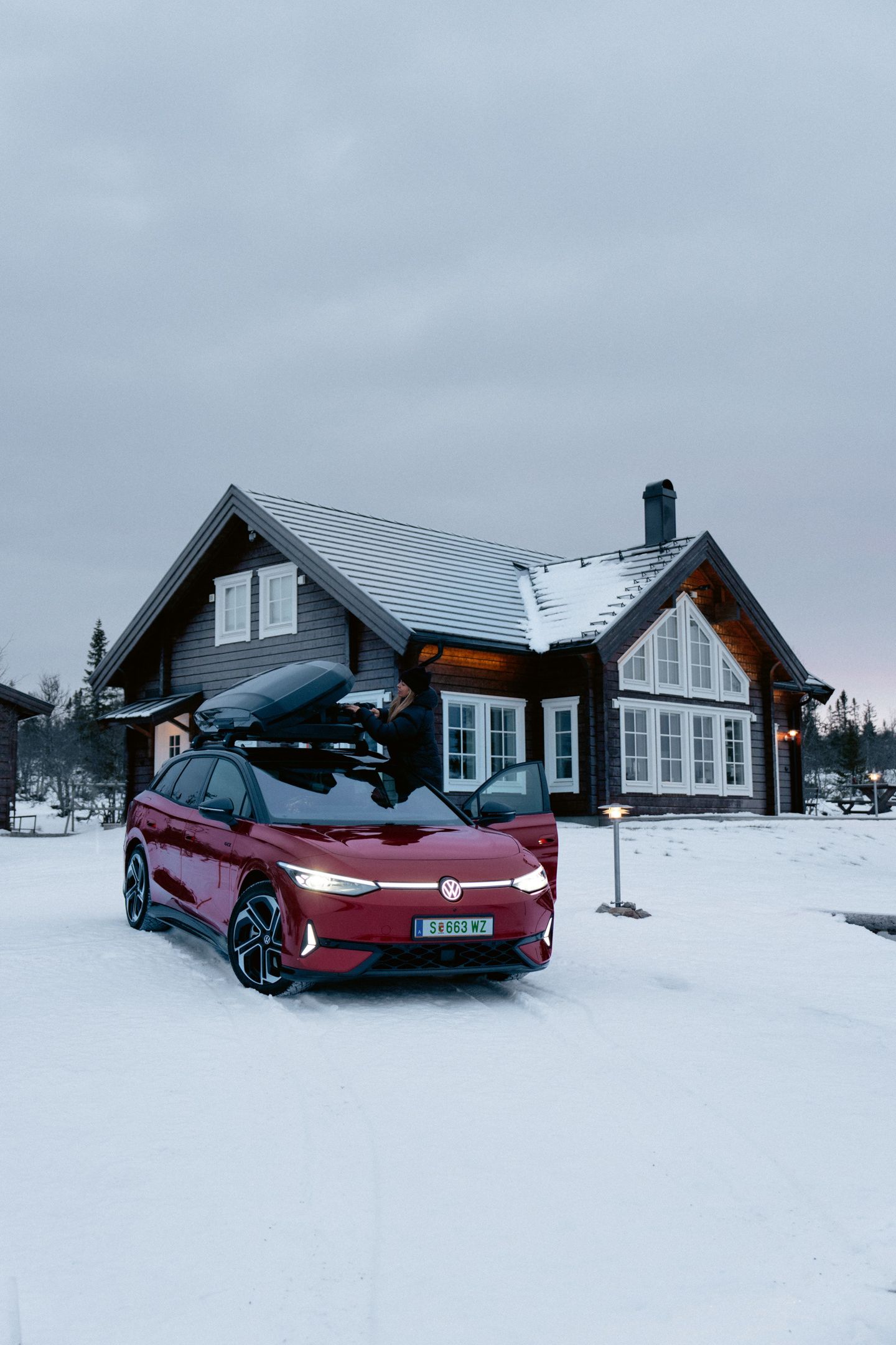 Ein roter ID.7 Tourer GTX mit Dachbox steht im Schnee vor einem Wohnhaus. 