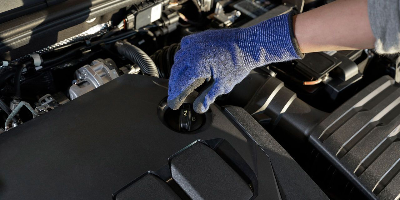 Block in den Motorraum eines Volkswagen. Eine Hand greift zum Ölmessstab.