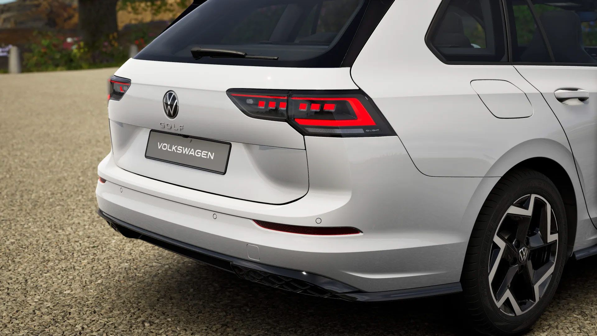 Heckansicht eines weißen Volkswagen Golf Variant. Zu sehen sind das Rücklichtdesign, die VW-Embleme und das Modellkennzeichen. Das Auto steht auf einem kiesbedeckten Parkplatz.