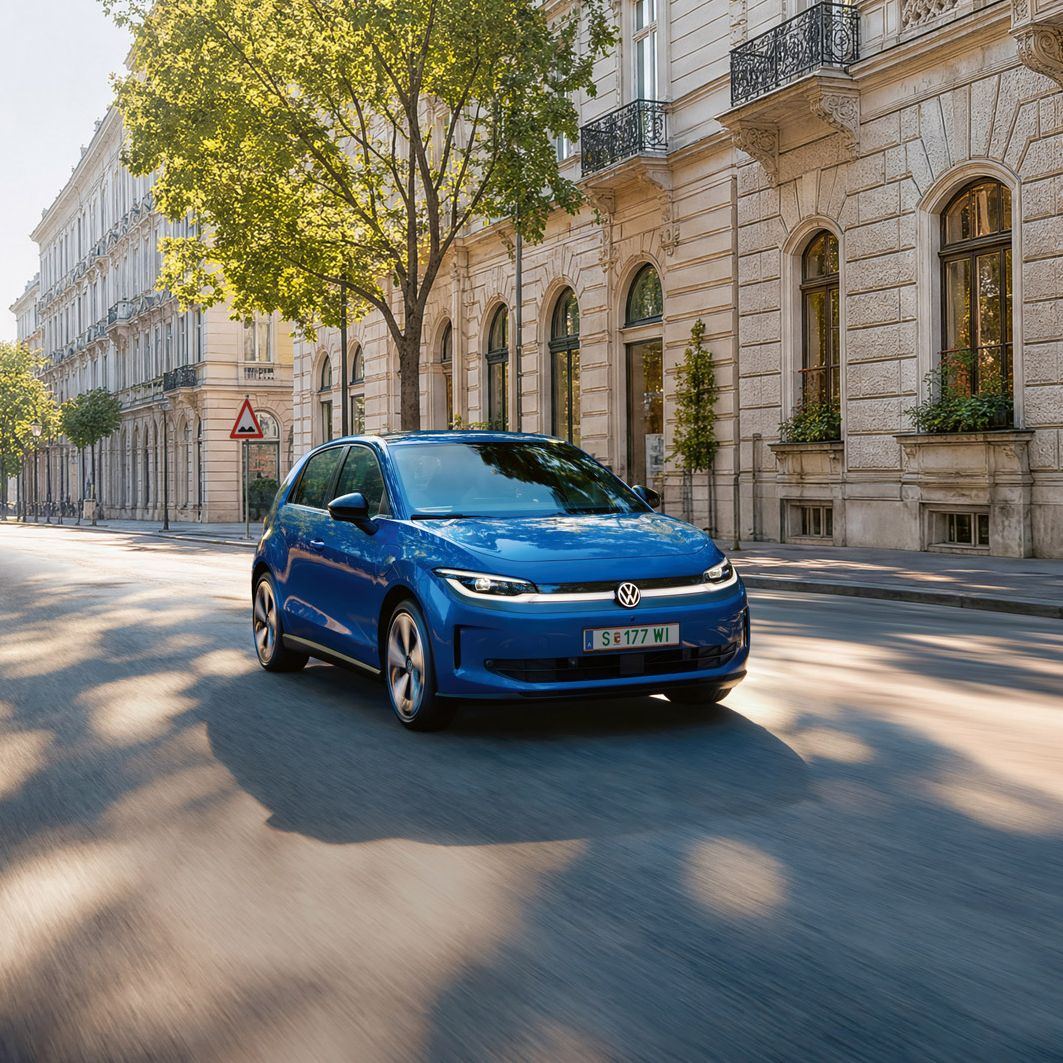 Ein blauer VW ID. Polo fährt auf einer breiten Straße im Schatten einer Allee.