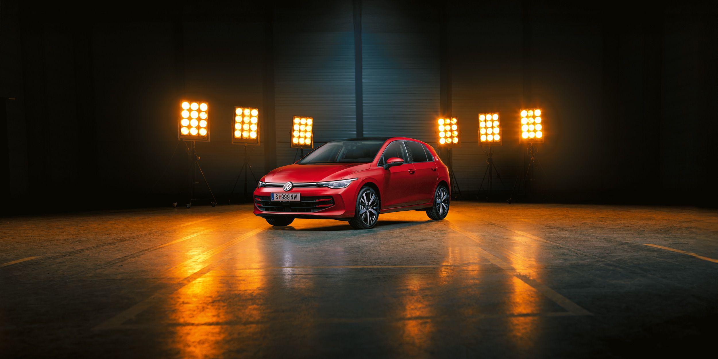 Ein roter Der VW Golf Falco Edition steht einer leeren Halle, dahinter Bühnenlicht.