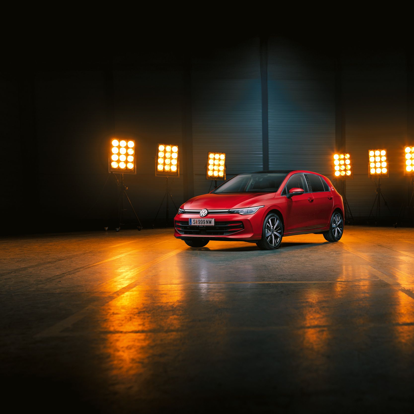 Ein roter Der VW Golf Falco Edition steht einer leeren Halle, dahinter Bühnenlicht.