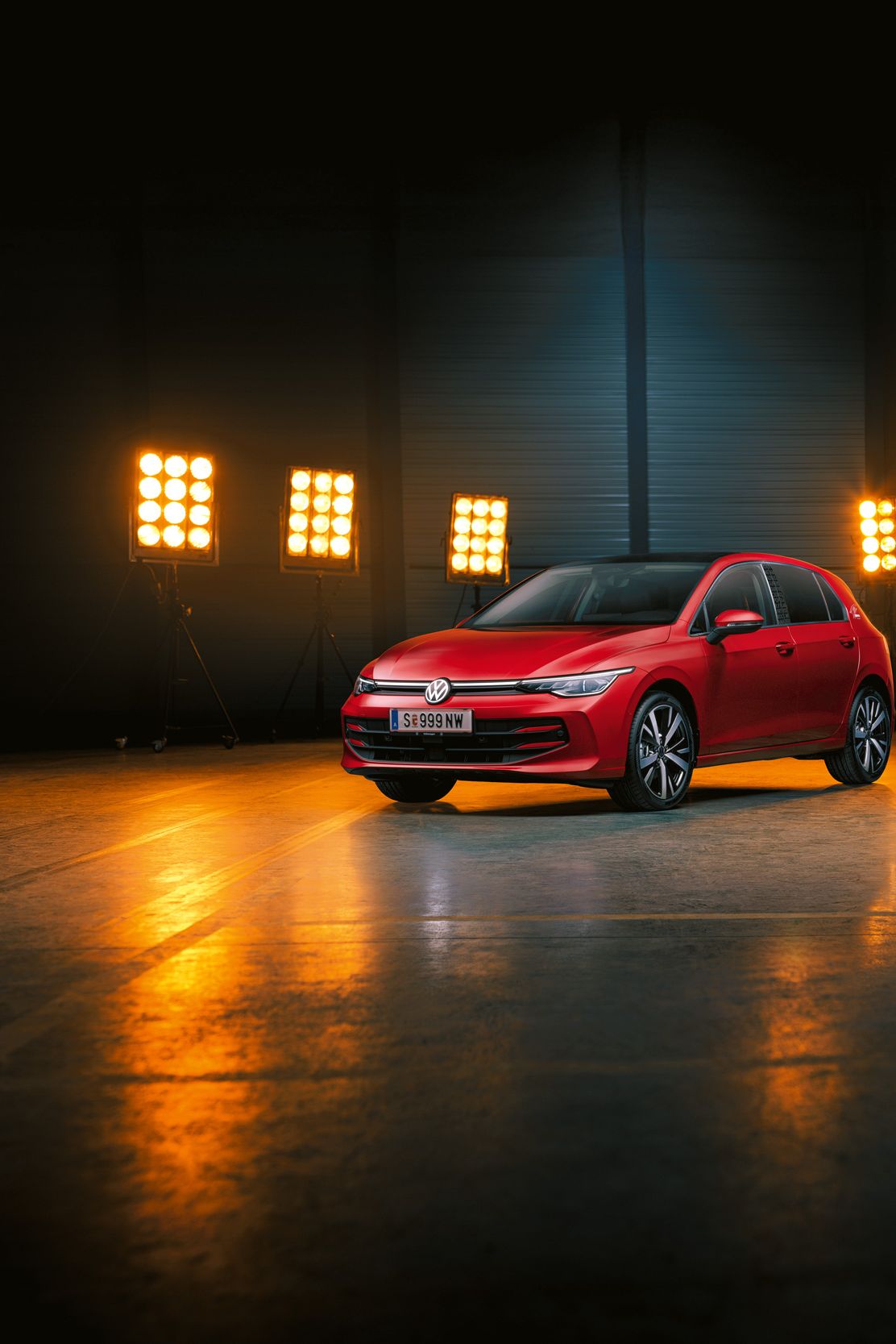 Ein roter Der VW Golf Falco Edition steht einer leeren Halle, dahinter Bühnenlicht.