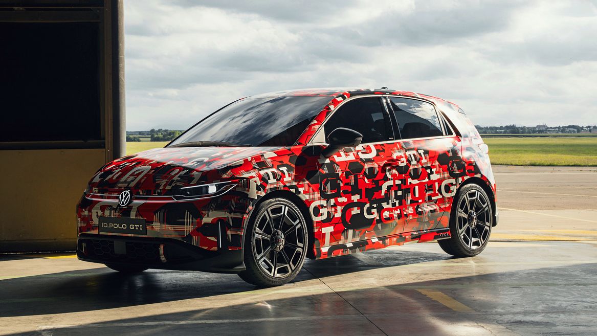 Ein ID. Polo GTI das mit Tarnmustern lackiert ist, steht in einer offenen Garage. Der Himmel im Hintergrund ist bewölkt. Die Lackierung könnte auf ein neues Modell oder eine Testversion hinweisen.