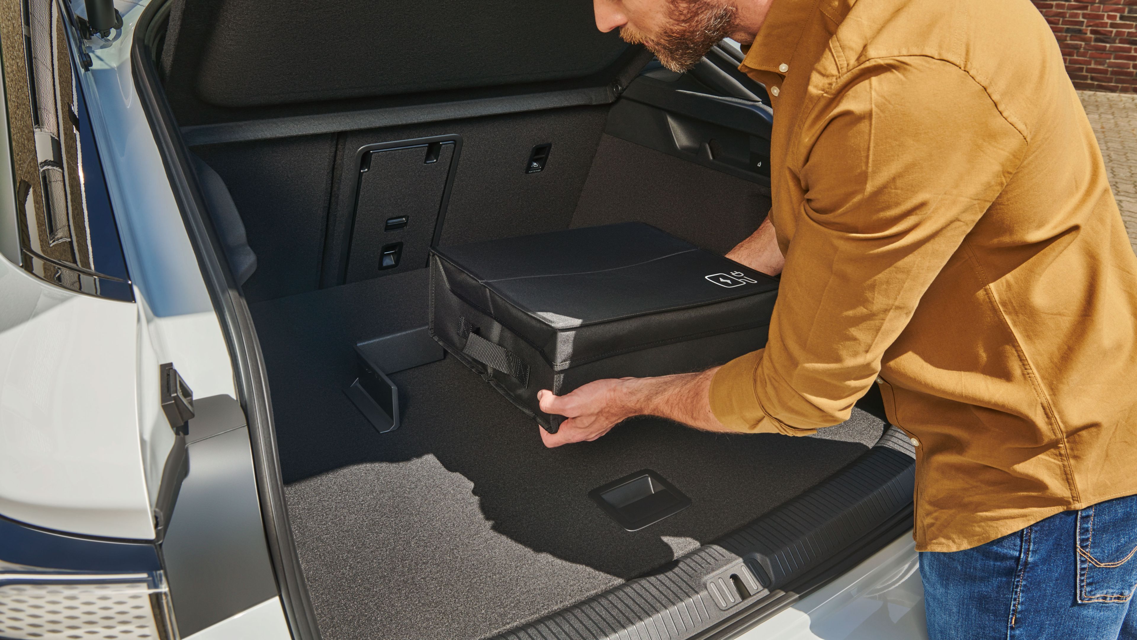 Ein Mann befestigt eine Tasche mit Volkswagen Original Cargo Elementen im Kofferraum eines Volkswagen ID.7.