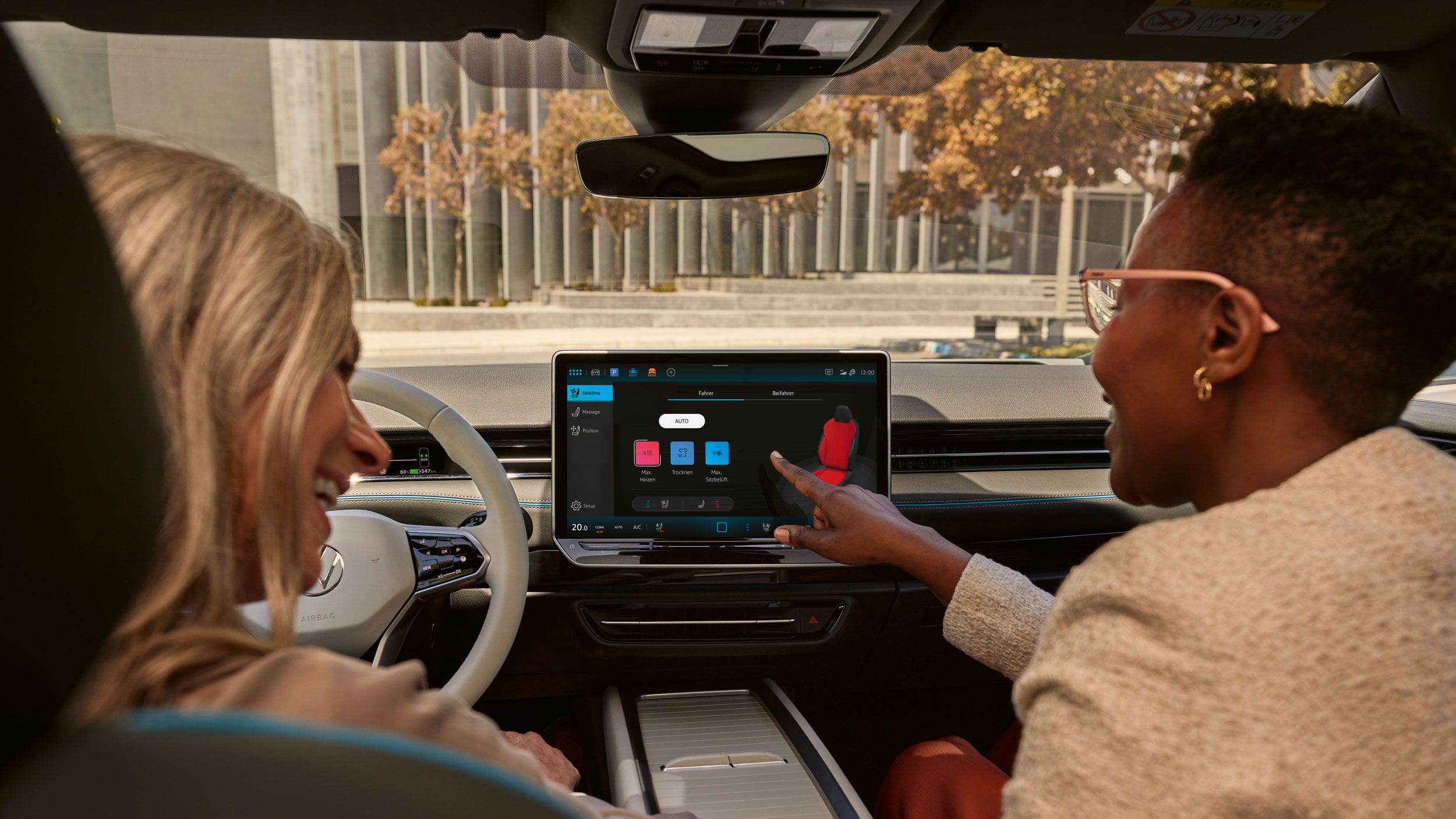 Zwei Frauen, die lachen, sitzen auf den Vordersitzen im VW ID.7 und bedienen das Infotainment-System.