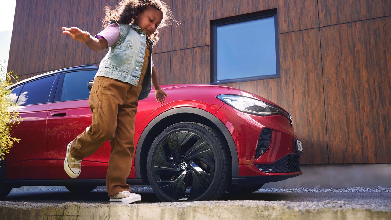 Ein Mädchen balanciert auf einem Mauervorsprung an einem roten Volkswagen vorbei.