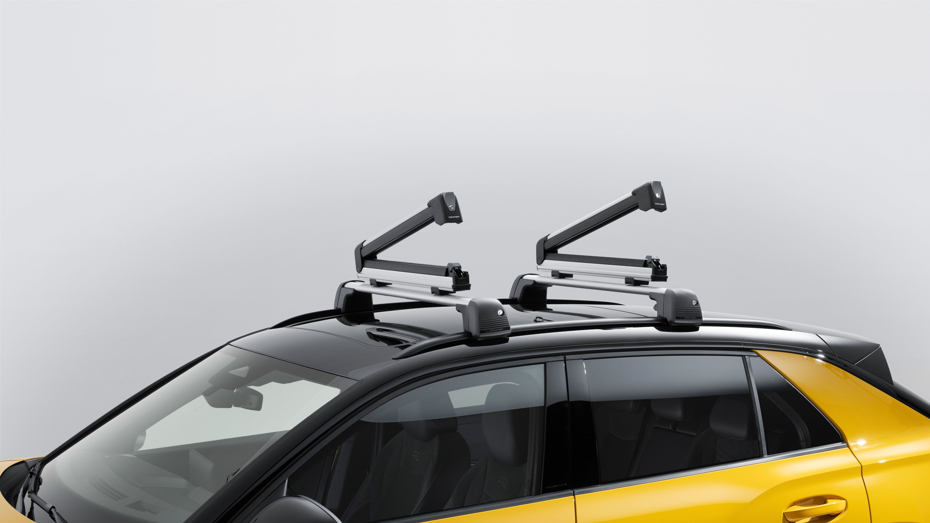 Geöffnete Volkswagen Ski- und Snowboardhalte am Dach eines gelben Volkswagen T-Roc.