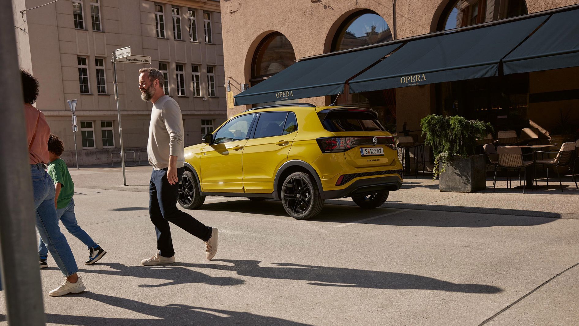 Ein gelber VW T-Cross parkt vor einem Café. Eine Familie geht davor über die Straße.
